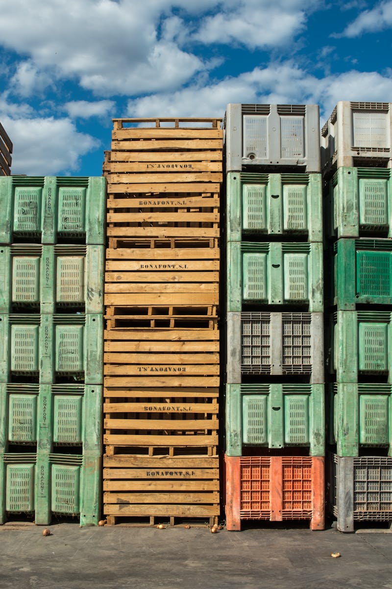 Stacks of wooden and plastic pallets under a blue sky, perfect for logistics and distribution themes.